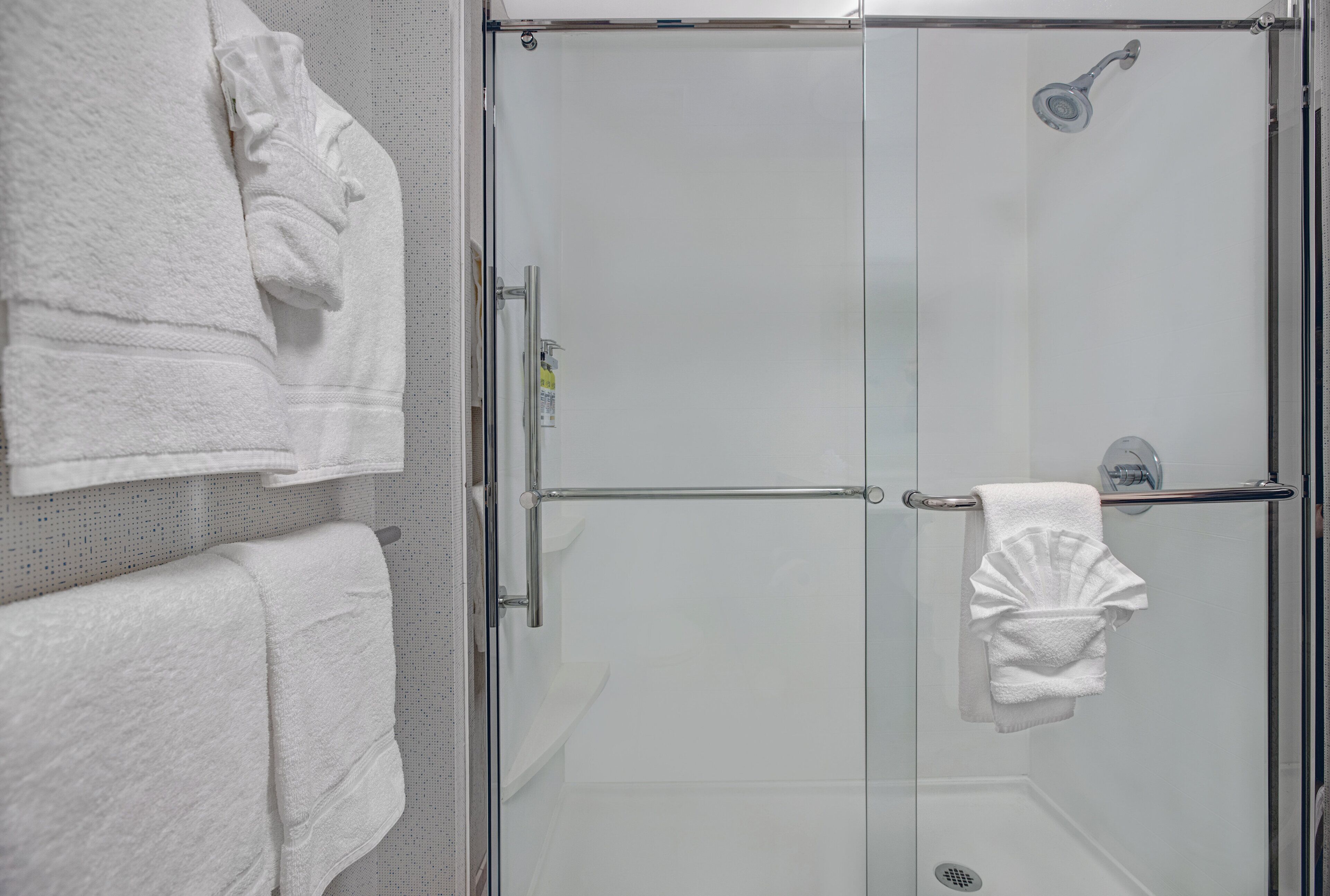 A glass-enclosed shower with a handheld showerhead, a towel rack, and a towel hanging on the wall.