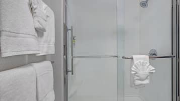 A glass-enclosed shower with a handheld showerhead, a towel rack, and a towel hanging on the wall.