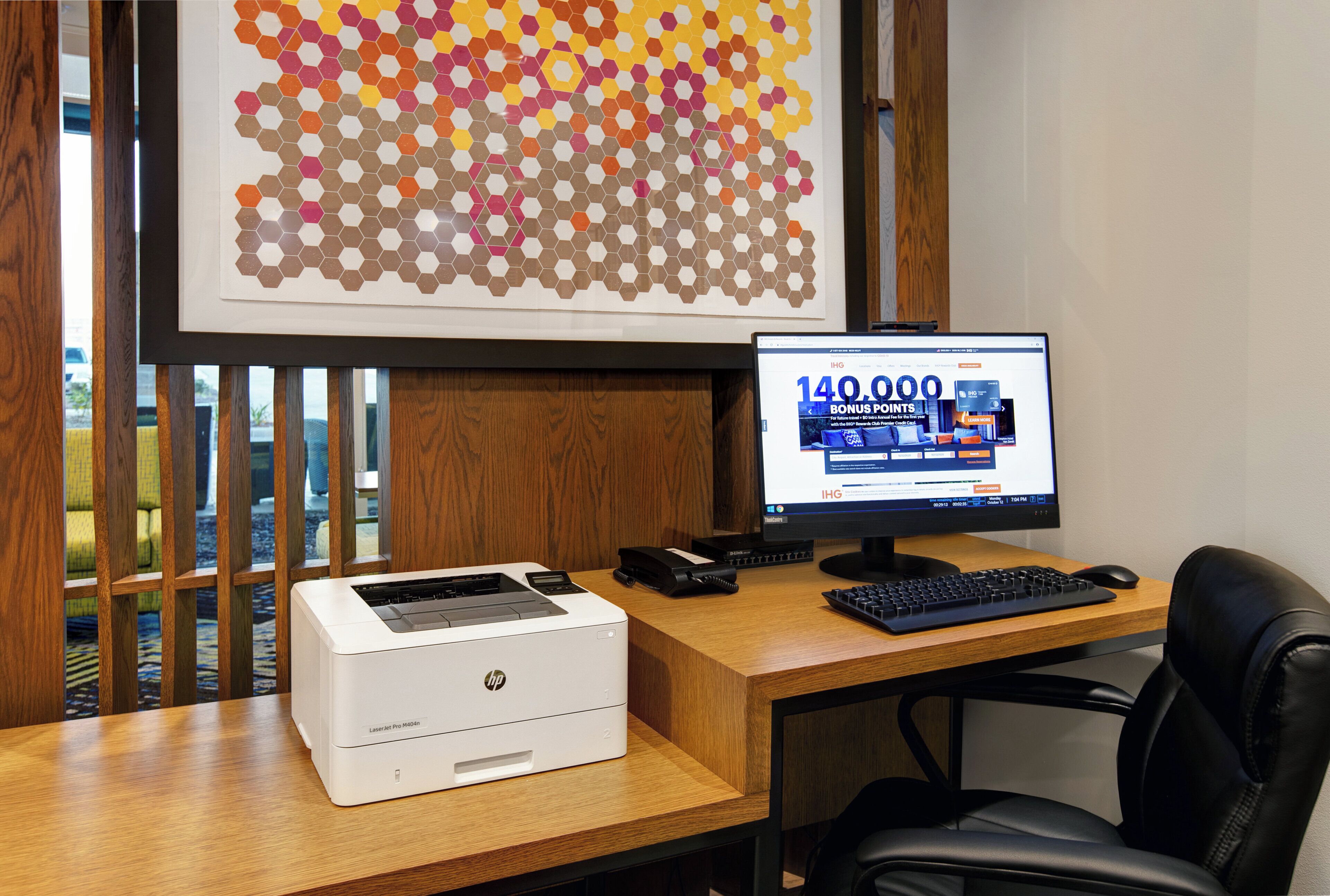 Een bureau met een HP LaserJet Pro M404n printer, een computermonitor waarop een webpagina wordt weergegeven, en een houten bureau met uitzicht op het buitengebied.