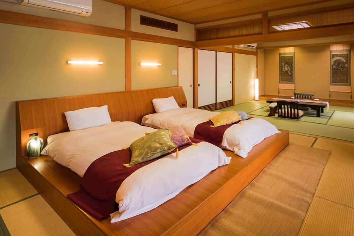 Una habitación tradicional japonesa con suelo de tatami, dos camas con almohadas, cabecero de madera y puerta corredera.