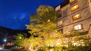 A building with multiple windows, a tree in front, and a starry night sky. - Unzen Shinyu (Unzen)