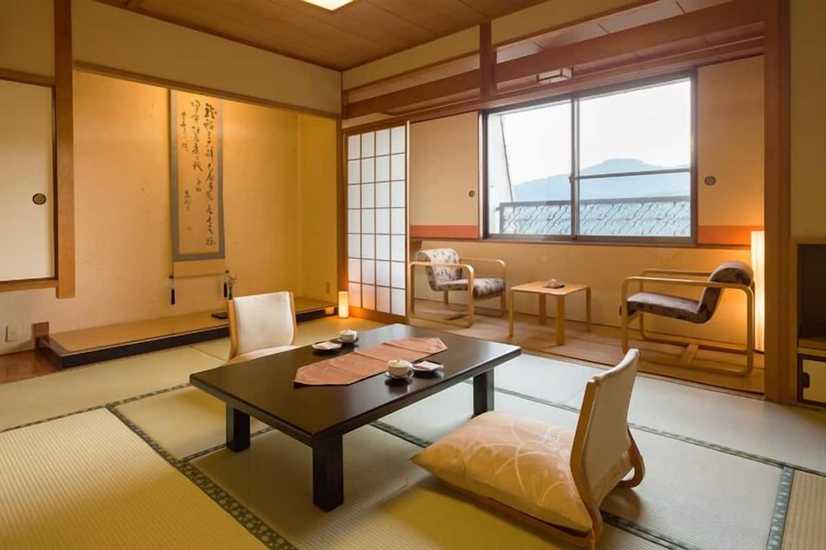 Una habitación japonesa tradicional con suelo de tatami, una mesa baja con cojines, una puerta corredera y vistas al mar.