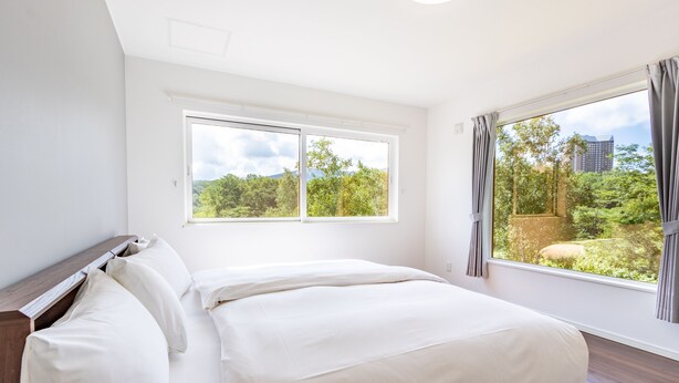 A bedroom with a large bed, two windows, and a view of greenery and a building. - Wapura Rusutsu (Rusutsu)