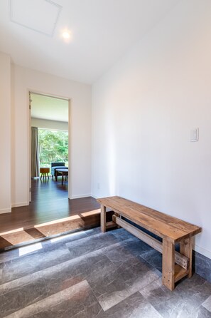 A hallway with a wooden bench, a door leading to a room with a table and chairs, and a view of greenery outside. - Wapura Rusutsu (Rusutsu)