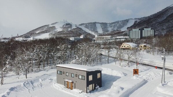A modern building with a flat roof and large windows, surrounded by snow-covered trees and a mountainous backdrop. - Wapura Rusutsu (Rusutsu)