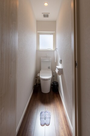 A narrow hallway with a toilet, a window, and a pair of slippers on the floor. - Wapura Rusutsu (Rusutsu)