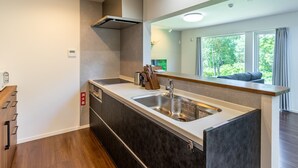 A modern kitchen with a large island, stainless steel appliances, and a view of the outdoors through large windows. - Wapura Rusutsu (Rusutsu)