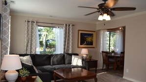 A living room with a black leather sofa, a wooden coffee table, a ceiling fan, and a dining area with a table and chairs.