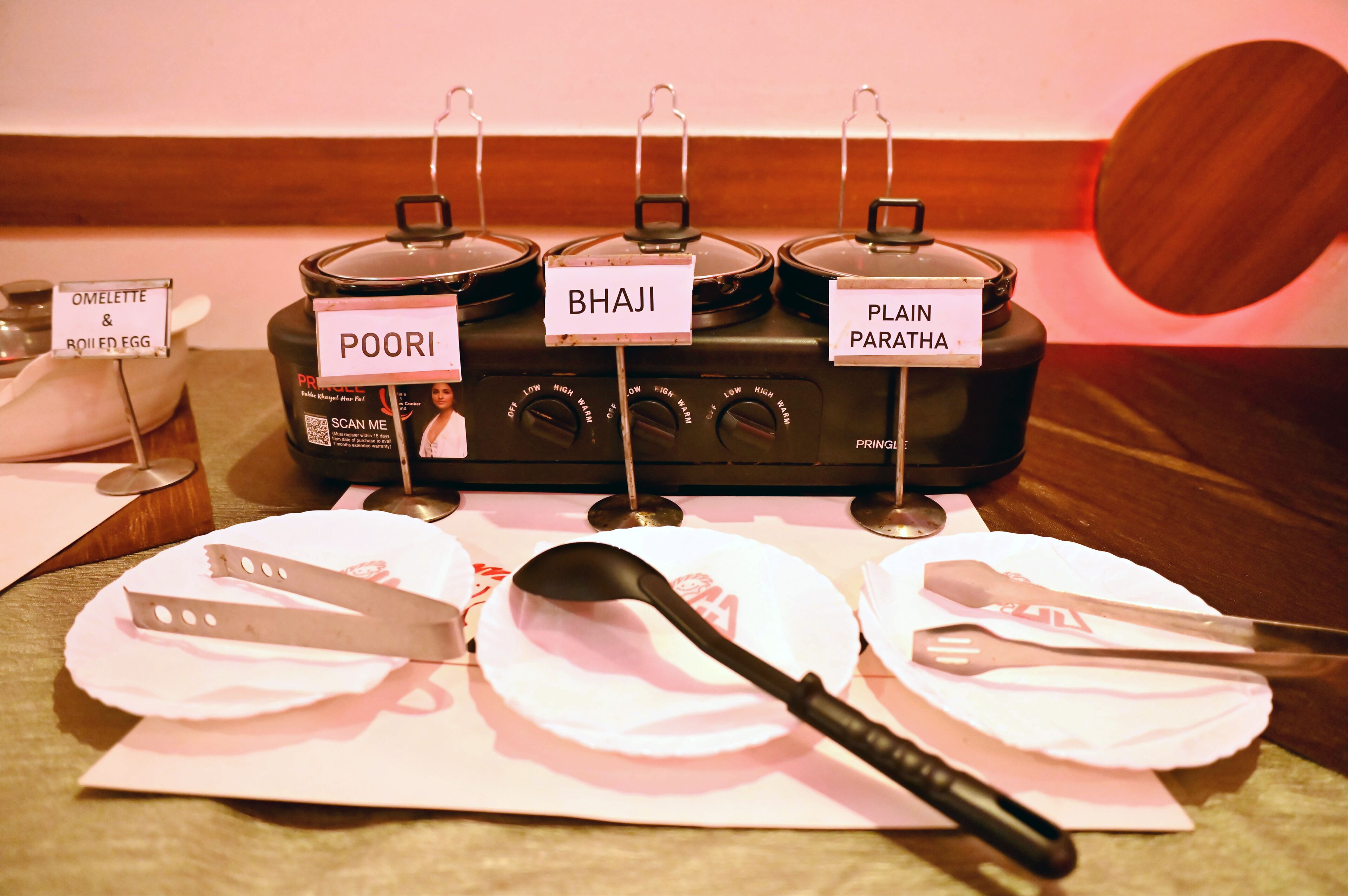 Buffet preparat amb recipients identificats per diferents plats, incloent truita i ou bullit, bhaji i paratha senzill.