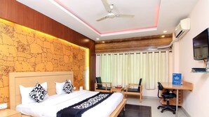 A modern hotel room with a large bed, a desk, a chair, a ceiling fan, and a TV. - Citi Club (Kanpur)