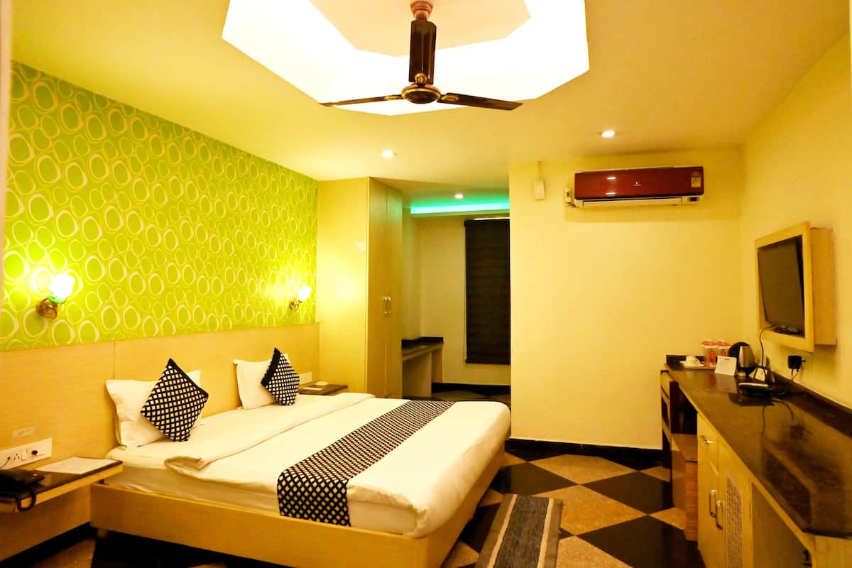 A hotel room with a bed, a desk, a television, and an air conditioning unit.