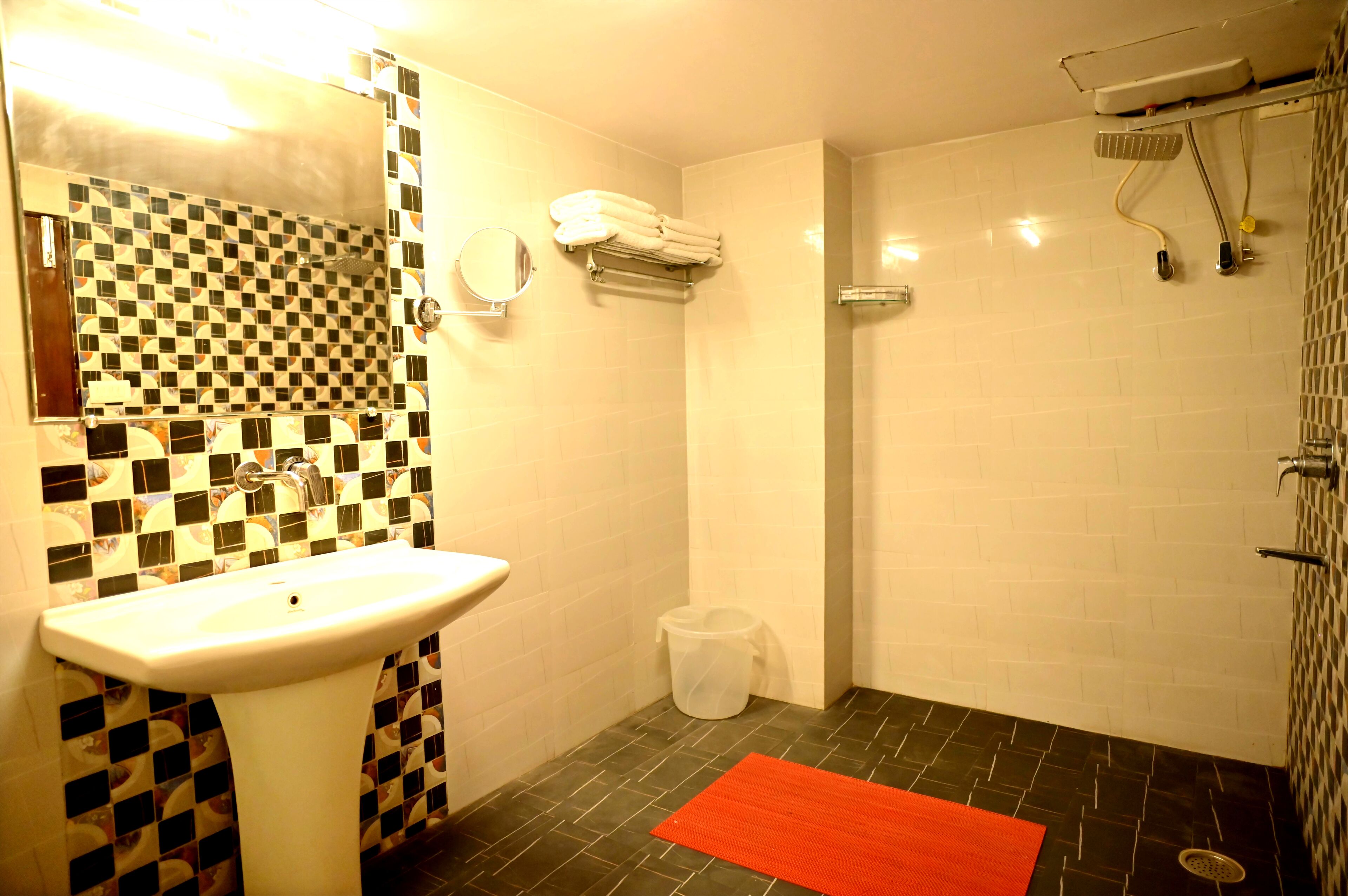 A bathroom with a sink, mirror, towel rack, shower, and a red rug.