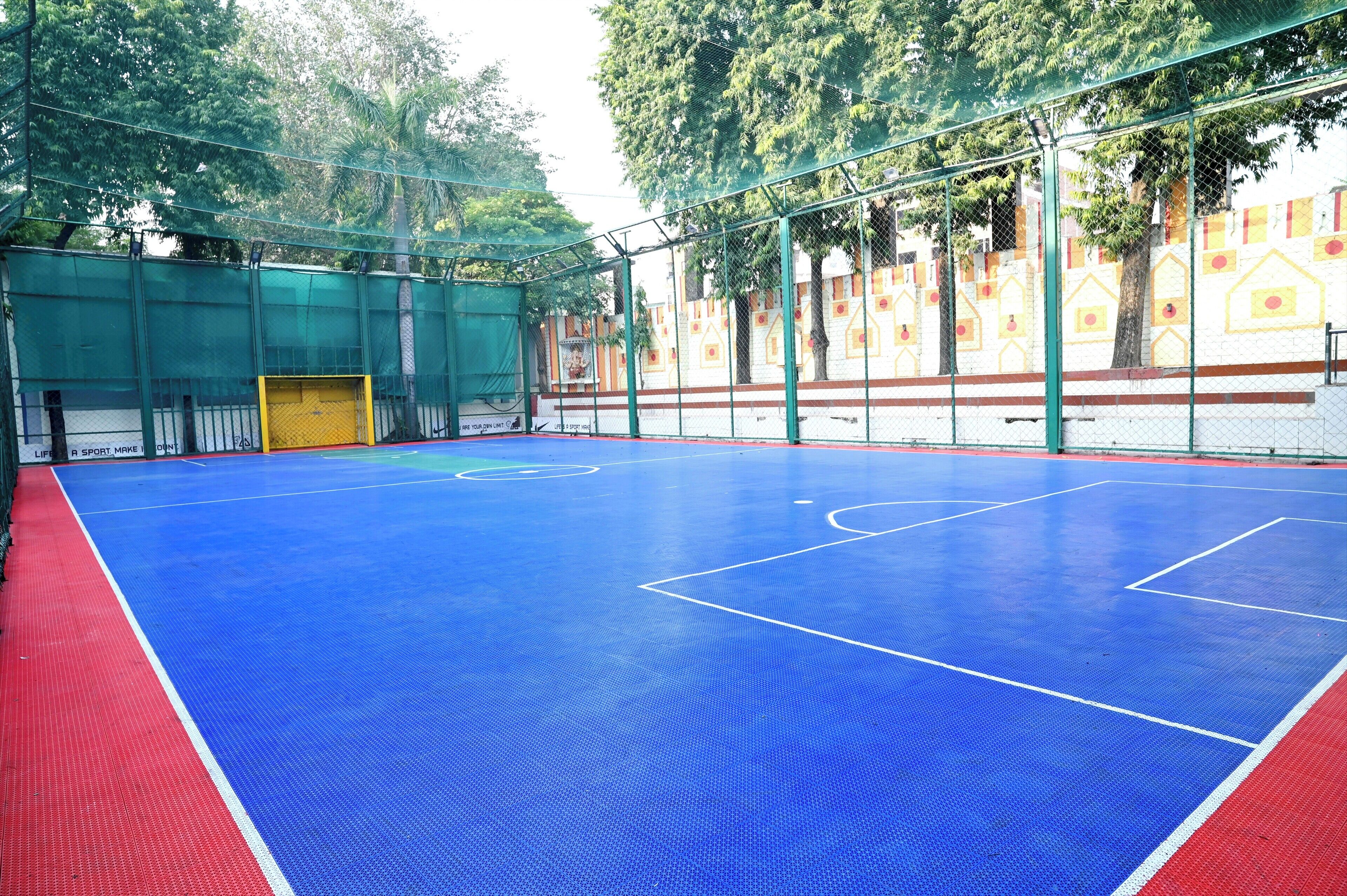An indoor sports court with a blue playing surface, surrounded by a green fence.