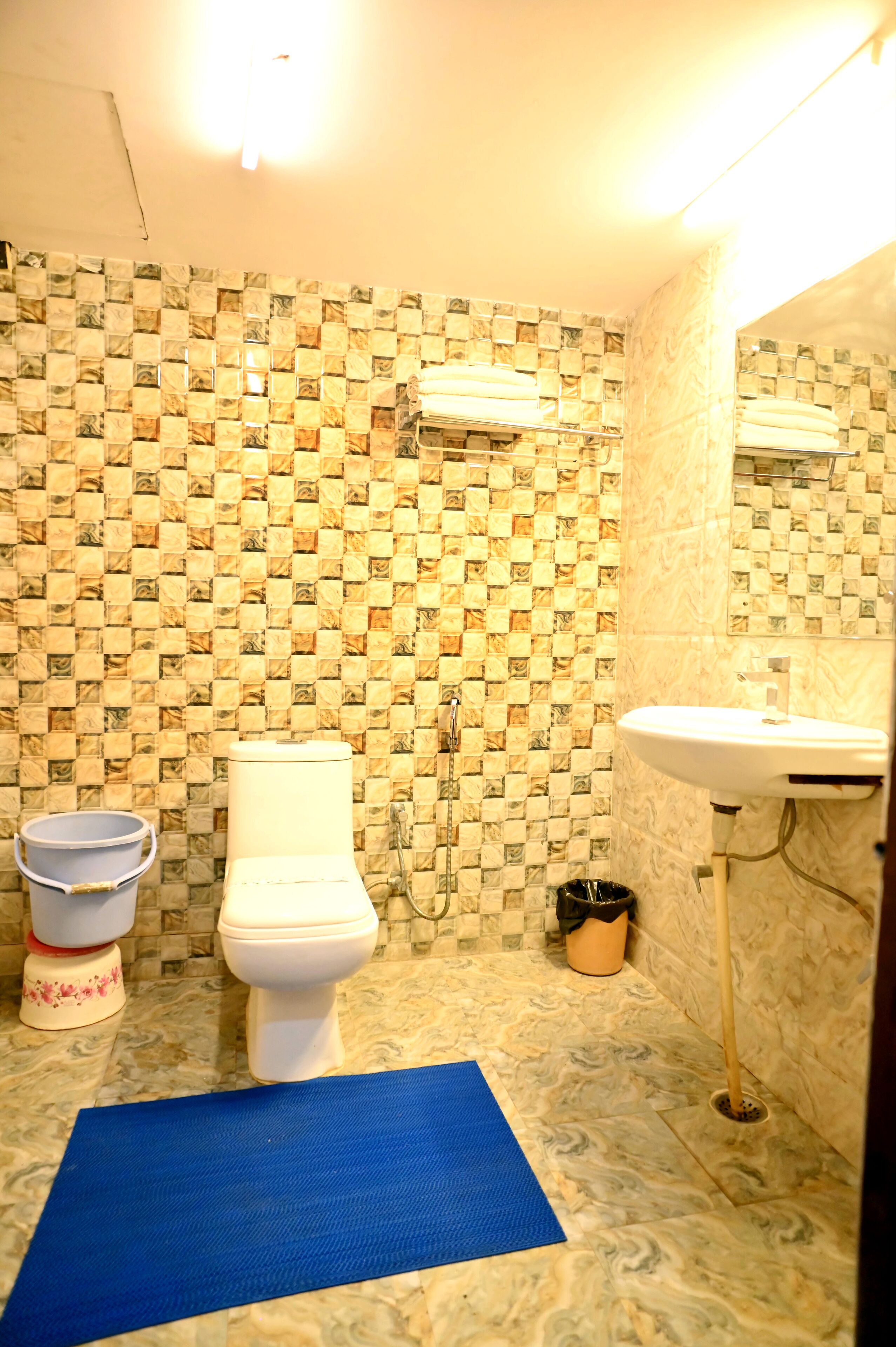 A bathroom with a tiled wall, a toilet, a sink, and a blue mat on the floor.