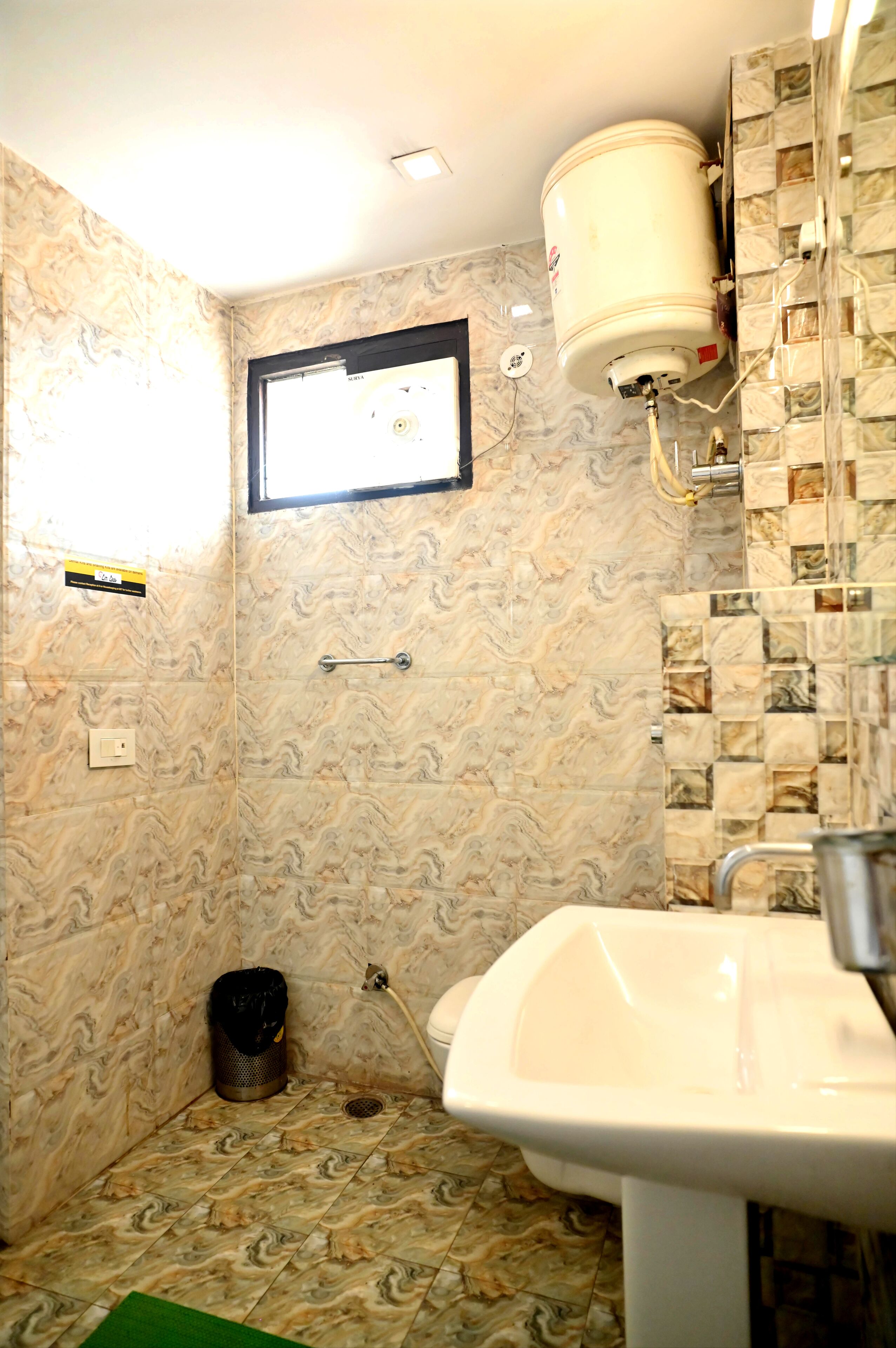 A bathroom with marble-patterned walls, a white sink, and a window above the toilet.