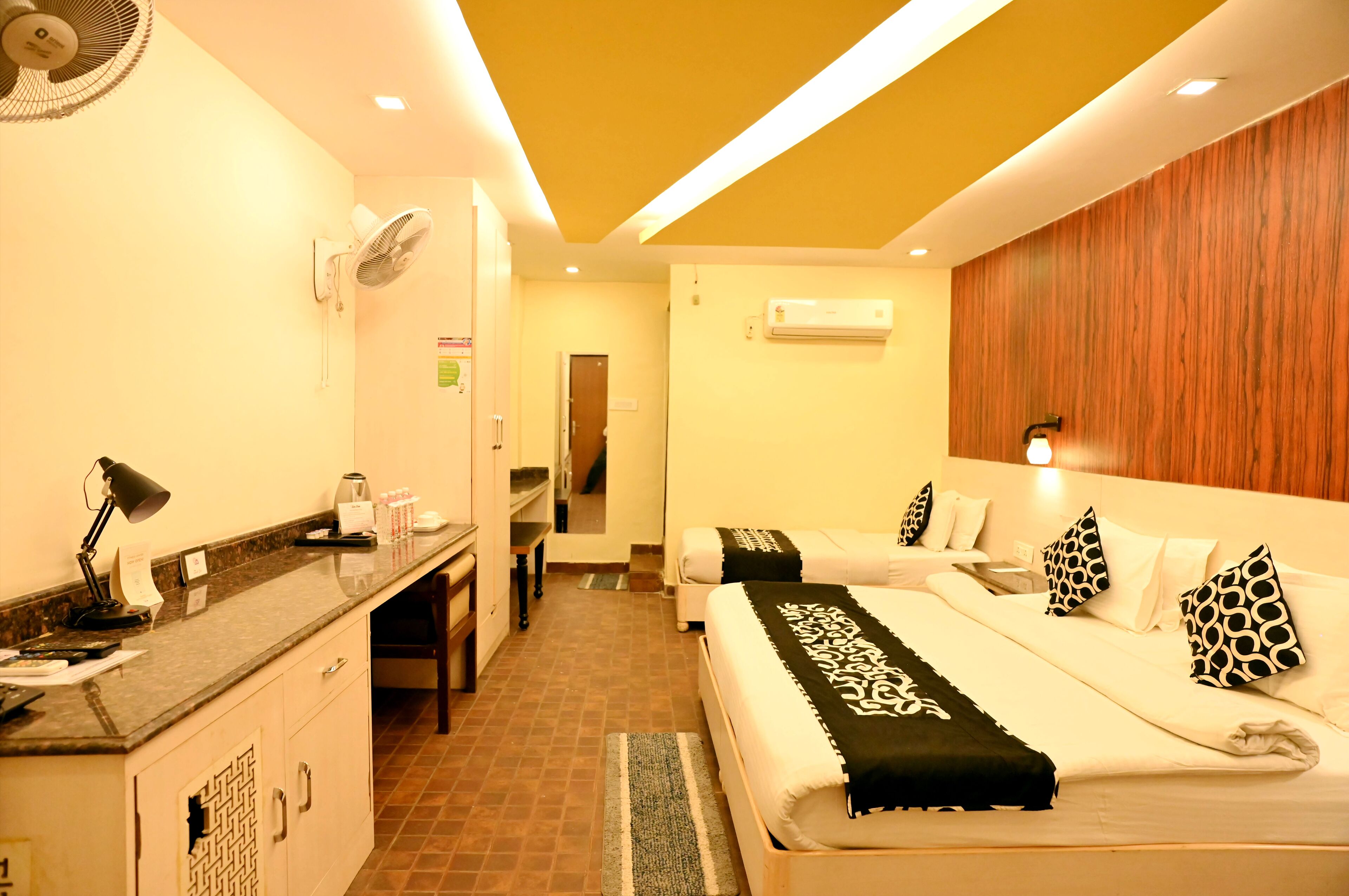 A hotel room with two beds, a desk with a lamp, a coffee maker, and an air conditioner.
