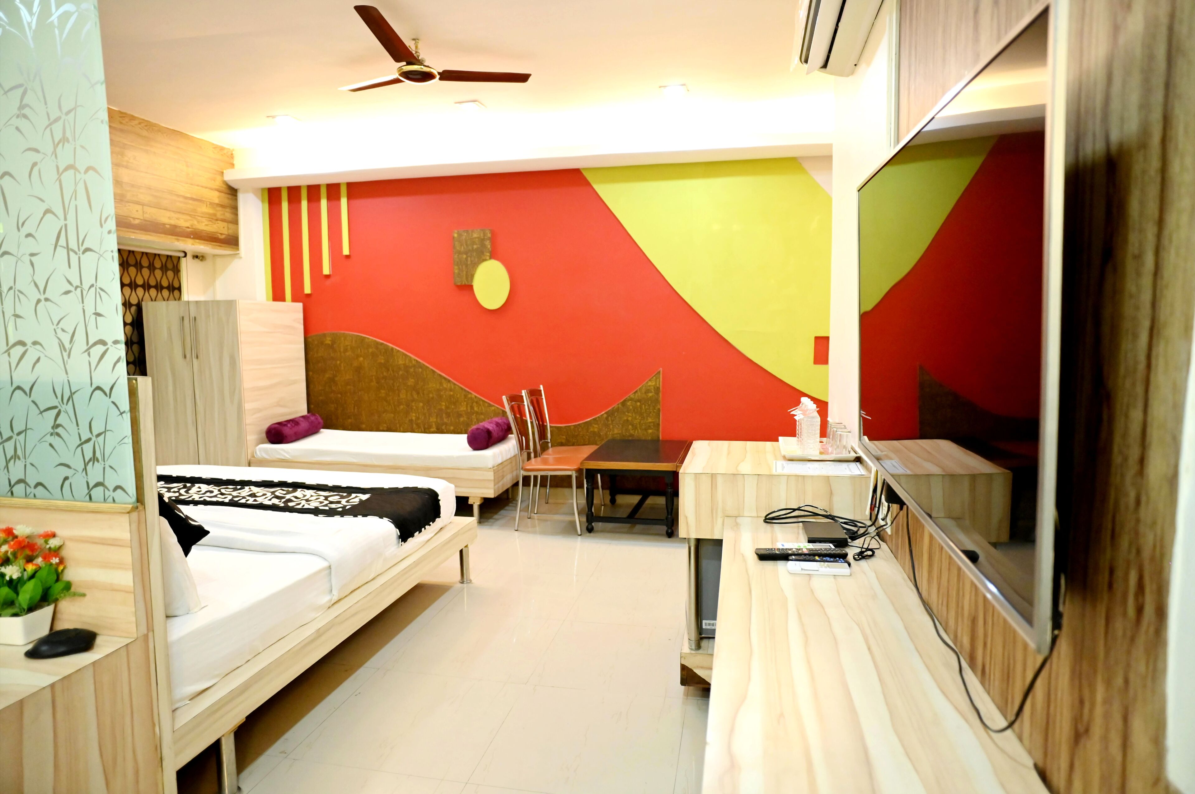 A hotel room with two beds, a dining table, a TV, and a ceiling fan.