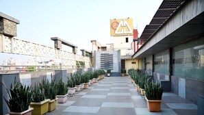 A rooftop terrace with potted plants arranged in rows, a modern building with a logo, and a clear sky. - Citi Club (Kanpur)