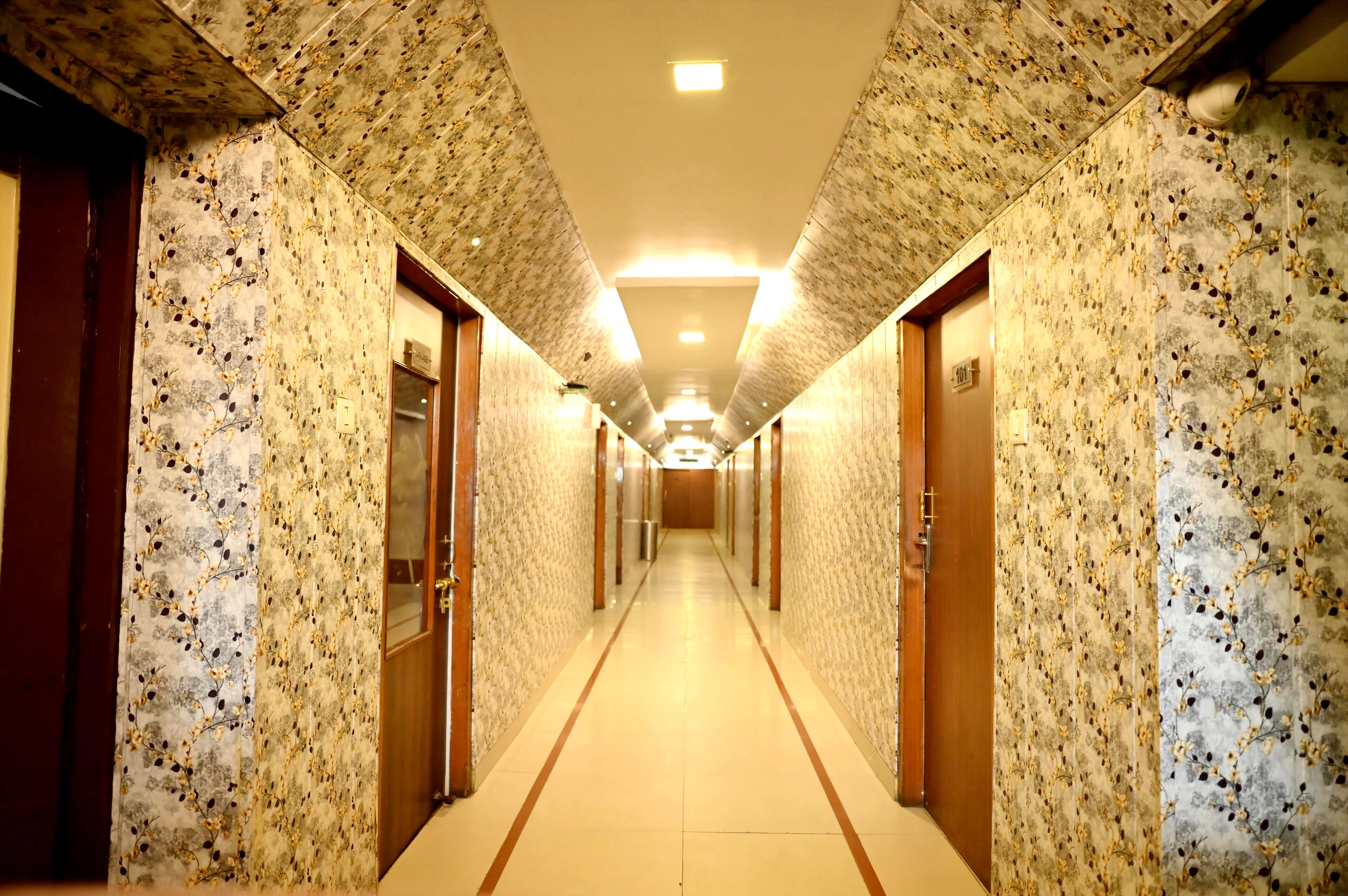 A long, narrow hallway with patterned walls and doors, leading to a bright, well-lit room at the end.