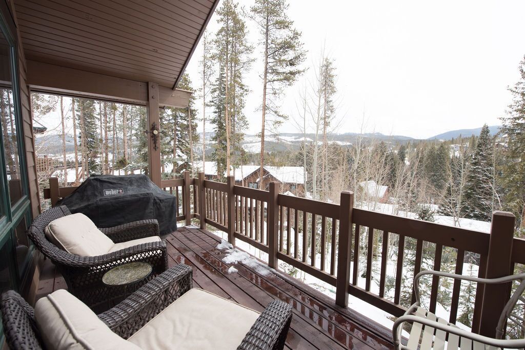 A covered outdoor seating area with wicker furniture and a view of snow-covered trees and mountains.