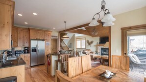 A spacious kitchen with wooden cabinets, a stainless steel refrigerator, and a dining area with a wooden table and chairs. - Walk to downtown Winter Park with views of Parry Peak (Winter Park)