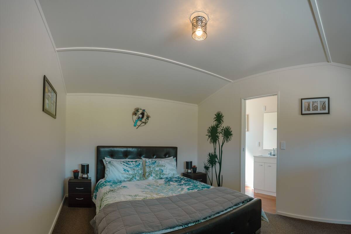Ein Schlafzimmer mit gewölbter Decke, einem Bett mit gestepptem Kopfteil, einem Nachttisch mit Lampe und einem Wandbild.