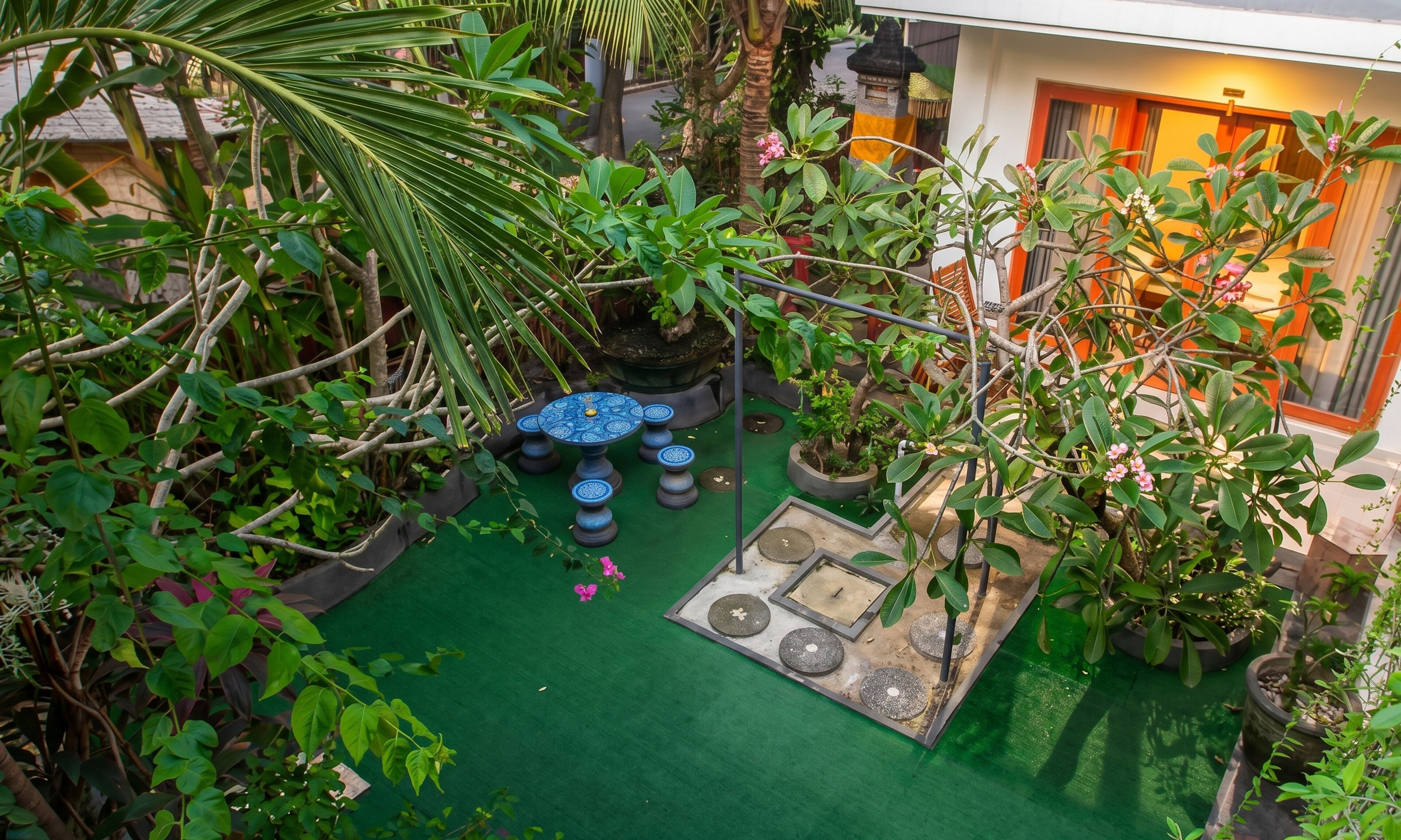 Un exuberante jardín con diversas plantas y un pequeño rincón de descanso con mesas de diseño azulado.