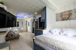 Une chambre d’hôtel moderne équipée d’un lit, d’un canapé, d’une télévision, d’une kitchenette et d’un coin repas.