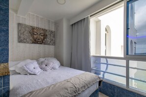 A bedroom with a bed, a large window, and a decorative wall piece.