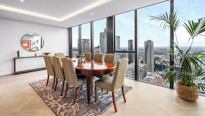 Un espace repas moderne avec vue sur la ville, comprenant une table ronde, six chaises, une grande fenêtre et une plante en pot.