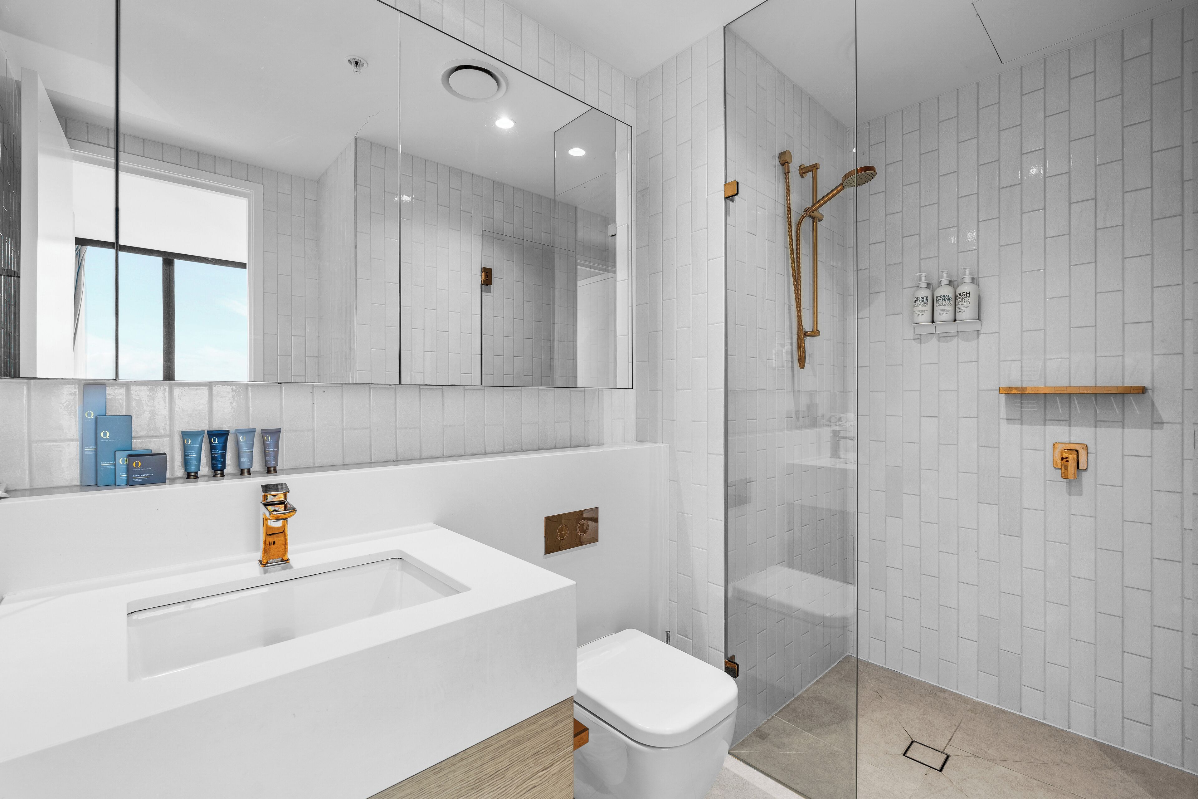Un baño moderno con un espejo grande, azulejos blancos, una bañera y una zona de ducha con mampara de vidrio.