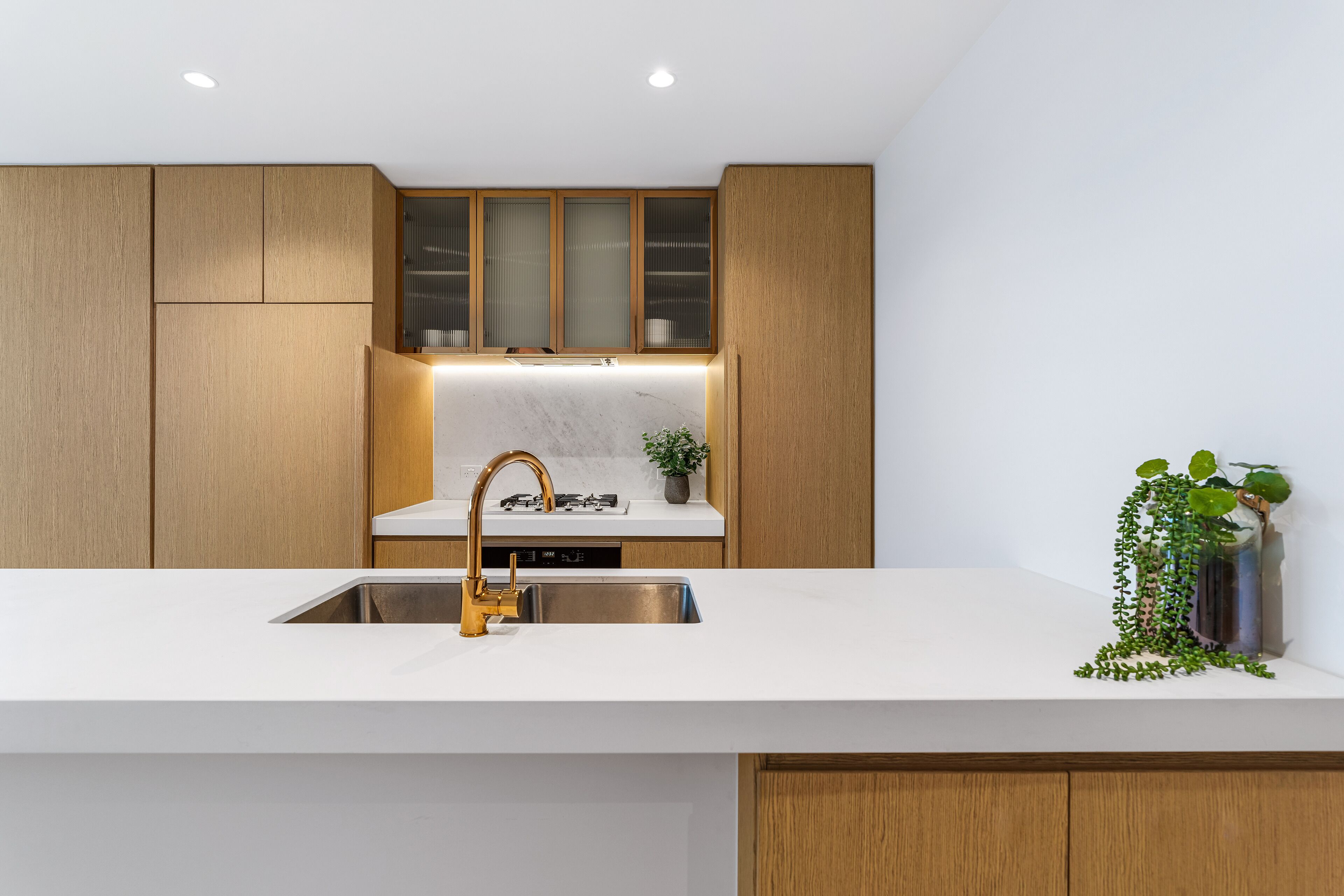 Une cuisine moderne avec des meubles en bois, un évier en acier inoxydable et un plan de travail blanc.