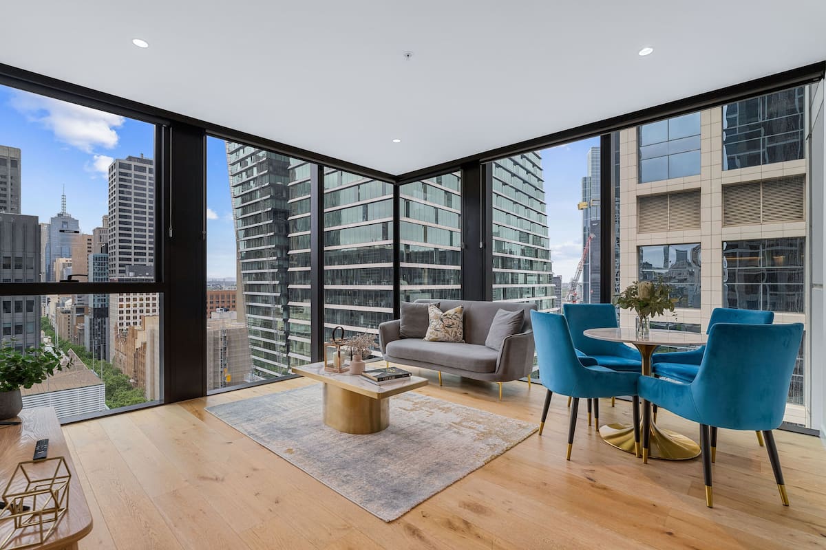 A modern living room with a sofa, two blue chairs, a coffee table, and a view of the cityscape through large windows.