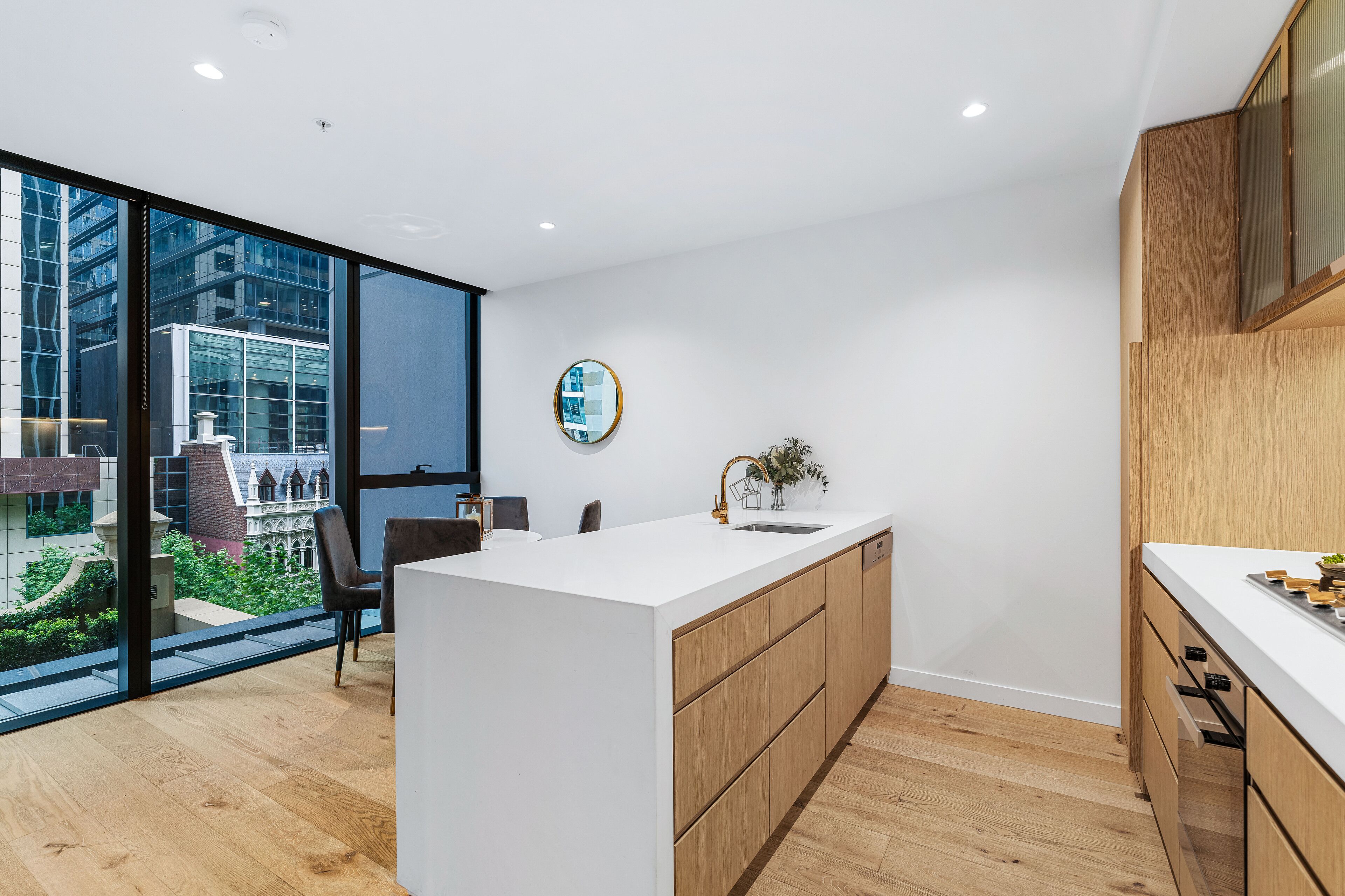 A modern kitchen with a large island, wooden cabinets, and a view of a cityscape through large windows.