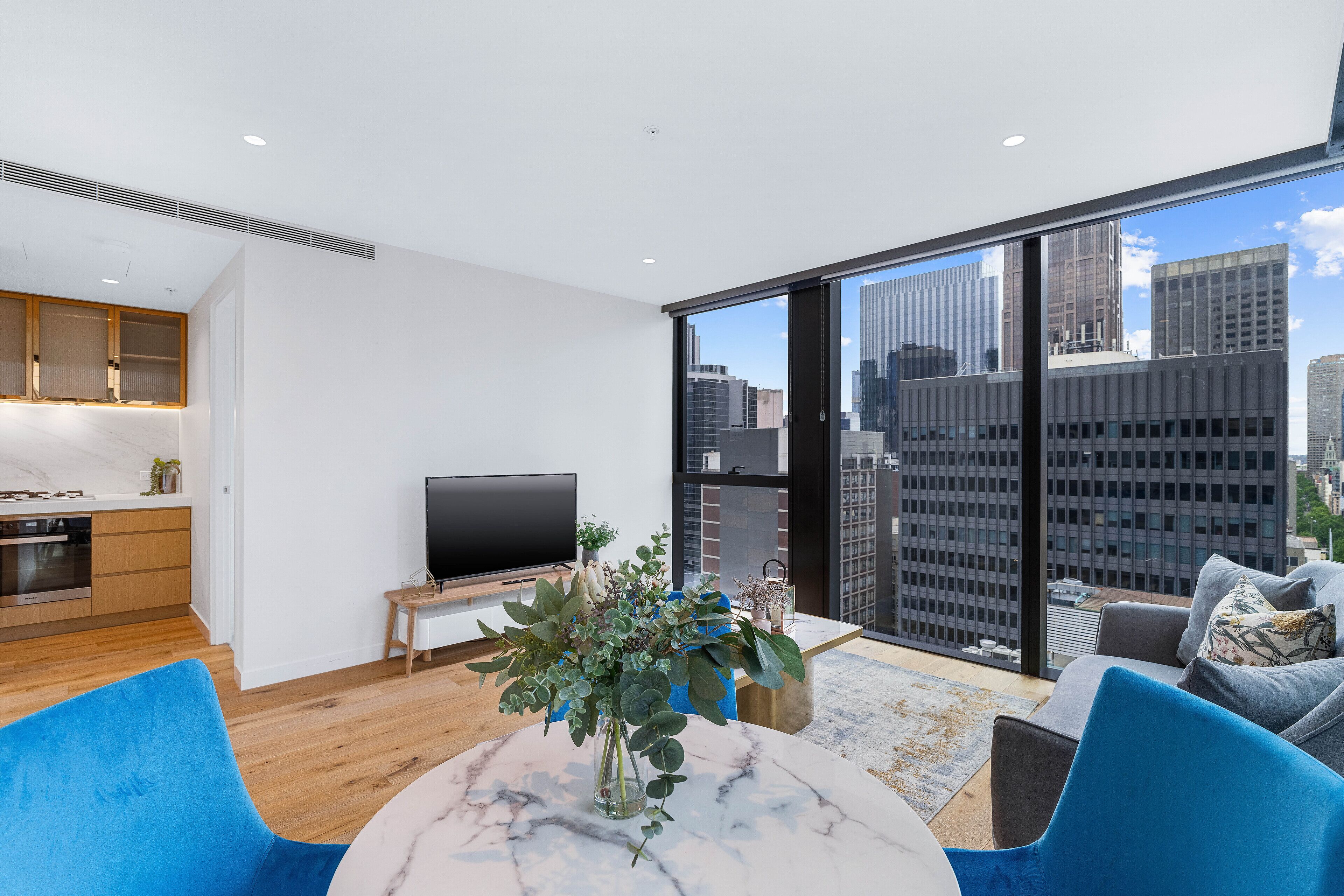 A modern living room with a city view, a kitchen area, and a dining space.