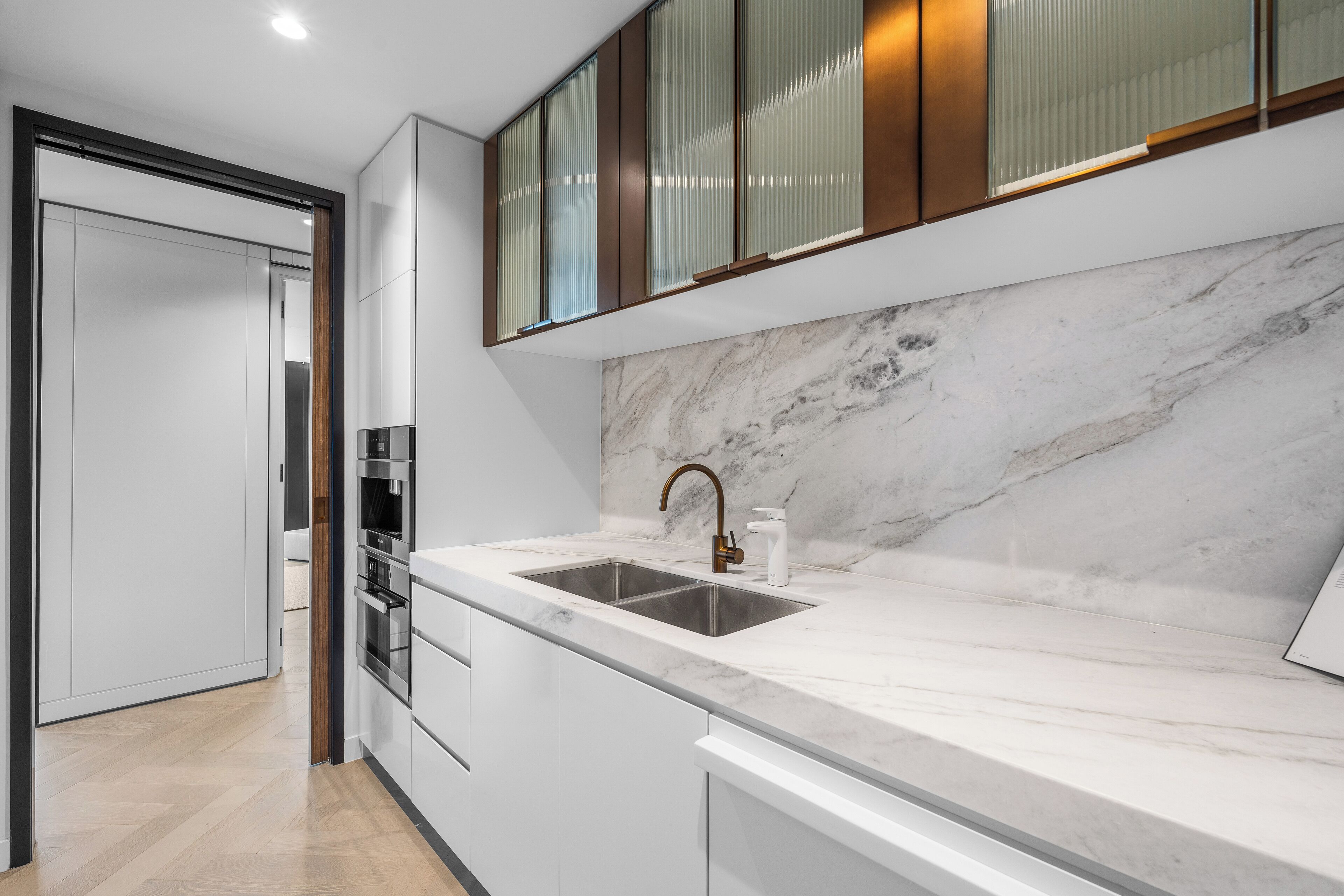 Una cocina moderna con encimera de mármol, pileta de acero inoxidable y horno empotrado.