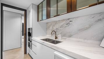 A modern kitchen with a marble countertop, stainless steel sink, and built-in oven.