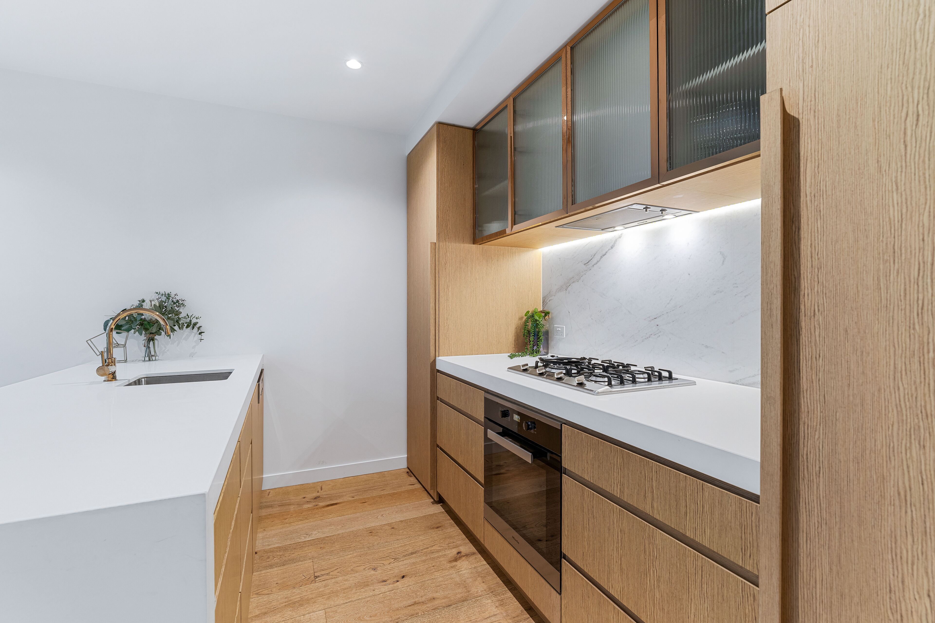 A modern kitchen with white countertops, wooden cabinets, and a built-in oven.