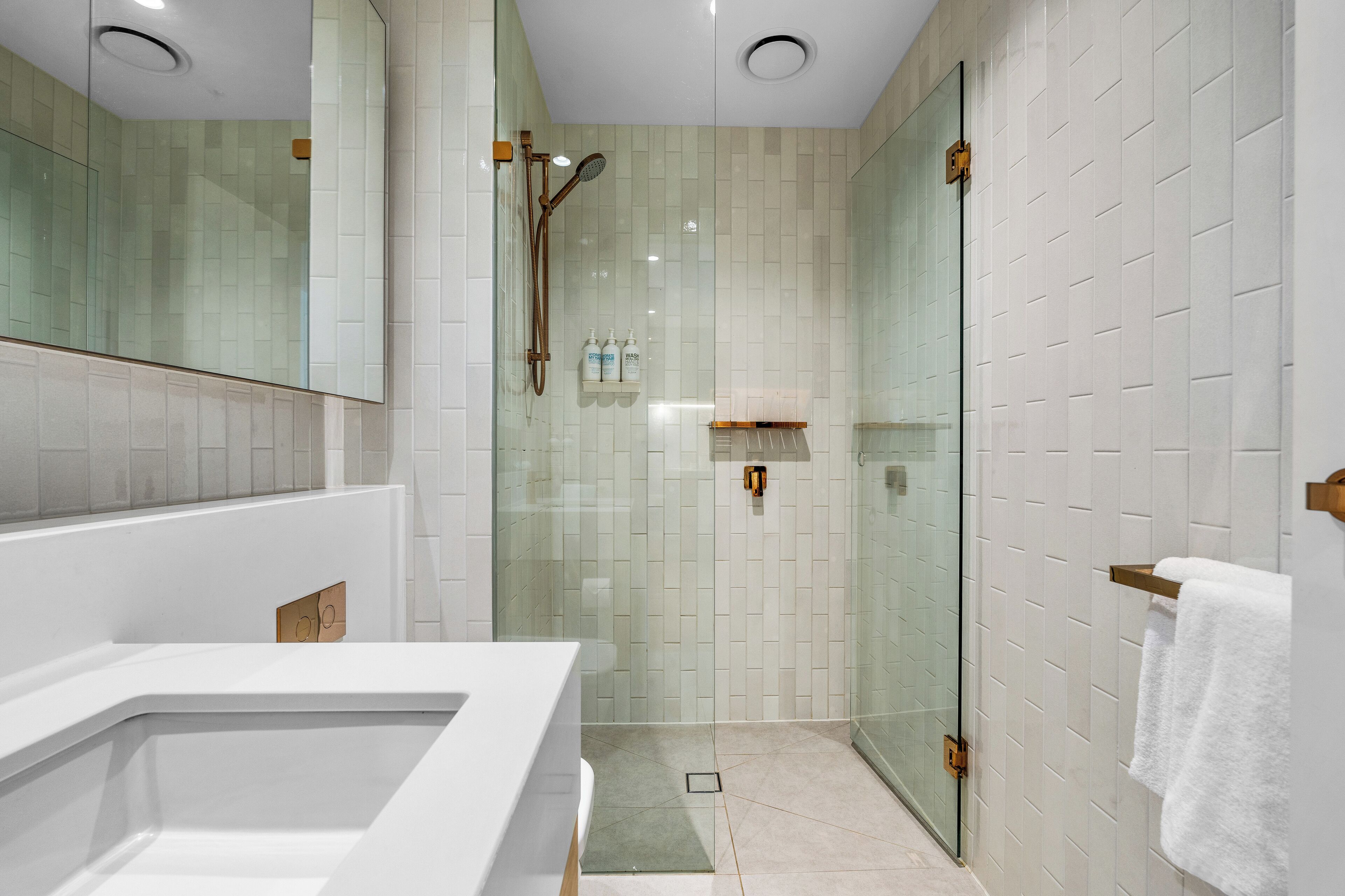 A modern bathroom with a glass shower enclosure, a large mirror, and a white sink.