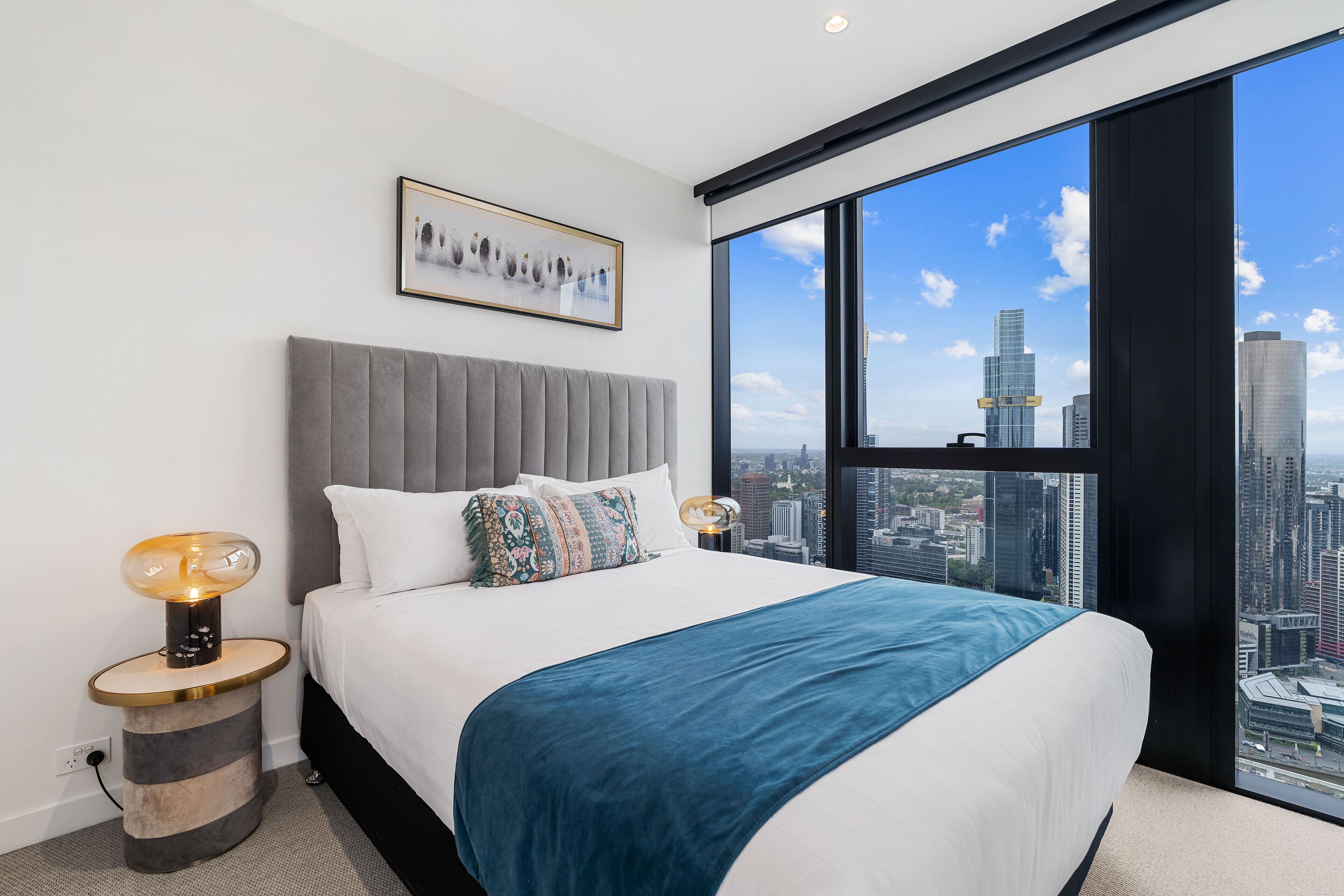 Une chambre moderne avec un grand lit, une vue sur la ville et une lampe de chevet originale.