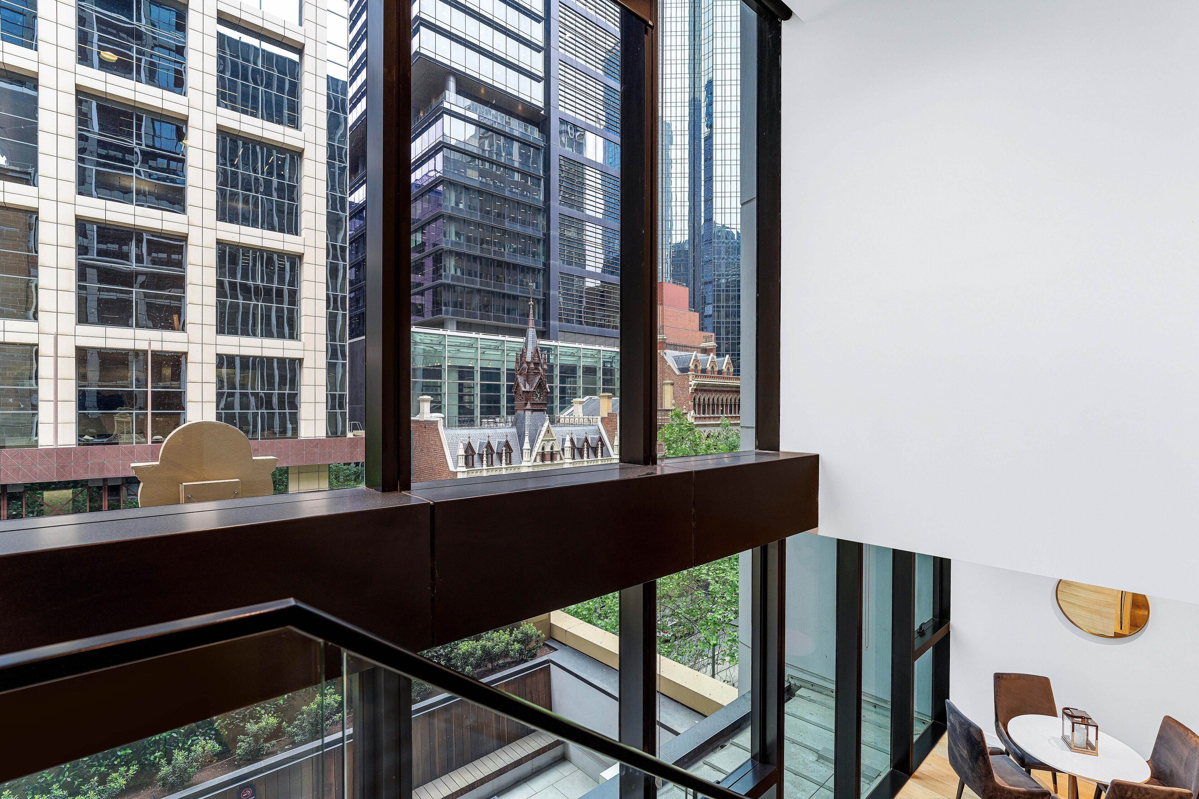 A modern hotel room with a large window offering a view of a cityscape, including high-rise buildings and a traditional building with a spire.