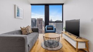 Un salon moderne avec un canapé gris, une table basse ronde, un fauteuil bleu et un téléviseur posé sur un meuble en bois.