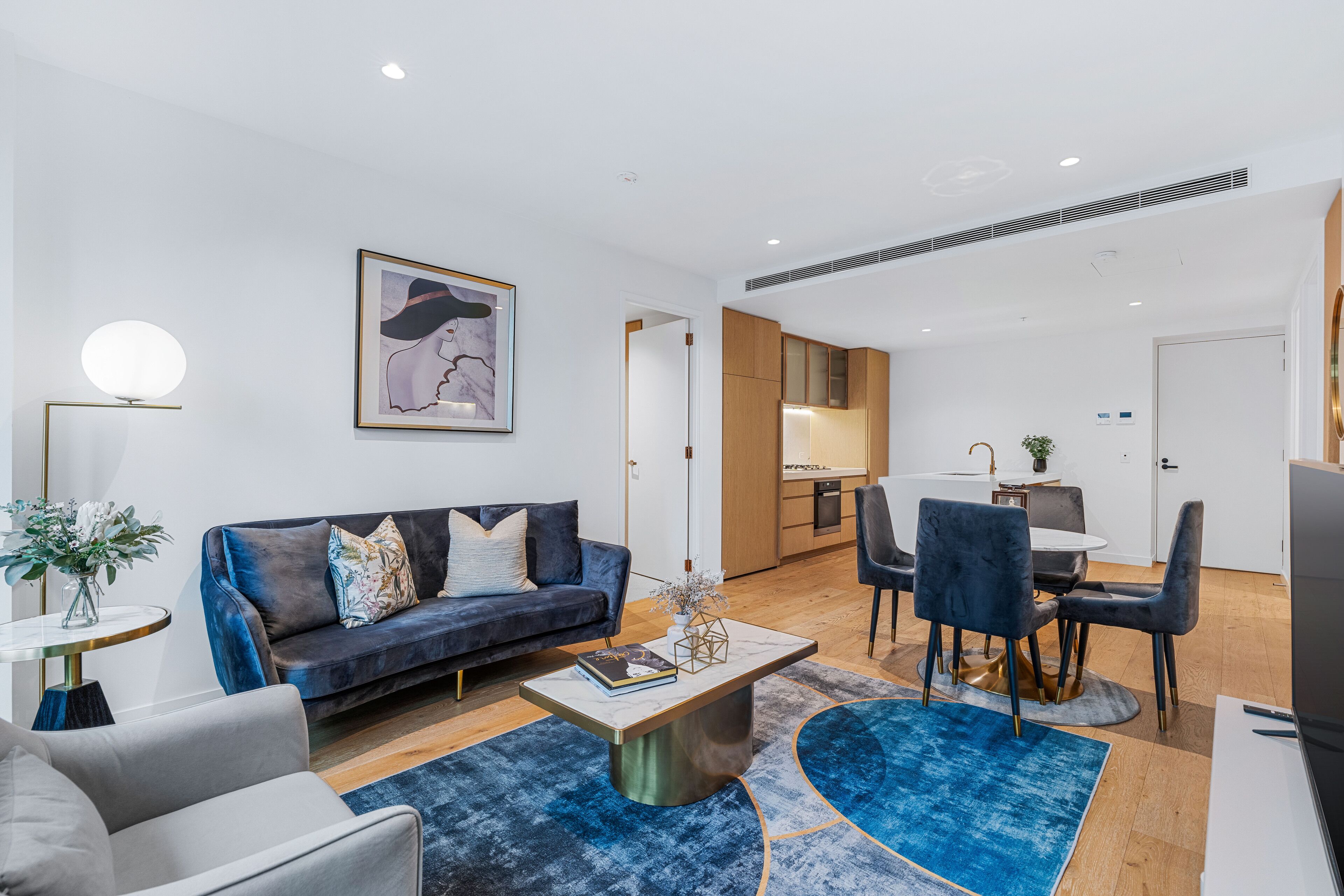 A modern living room with a dark blue sofa, a round coffee table, and a dining area with a small table and chairs.