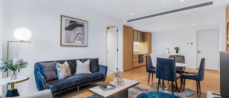 A modern living room with a dark blue sofa, a round coffee table, and a dining area with a small table and chairs.