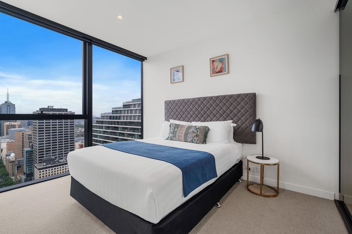 A modern hotel room with a large bed, a view of the city, and a small side table.