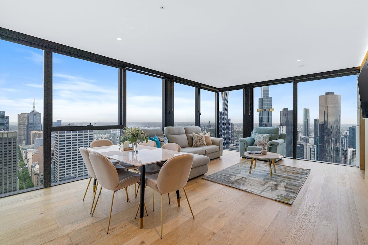 A spacious living room with a large city view, a dining area with a table and chairs, and a comfortable seating area with a sofa and armchairs.