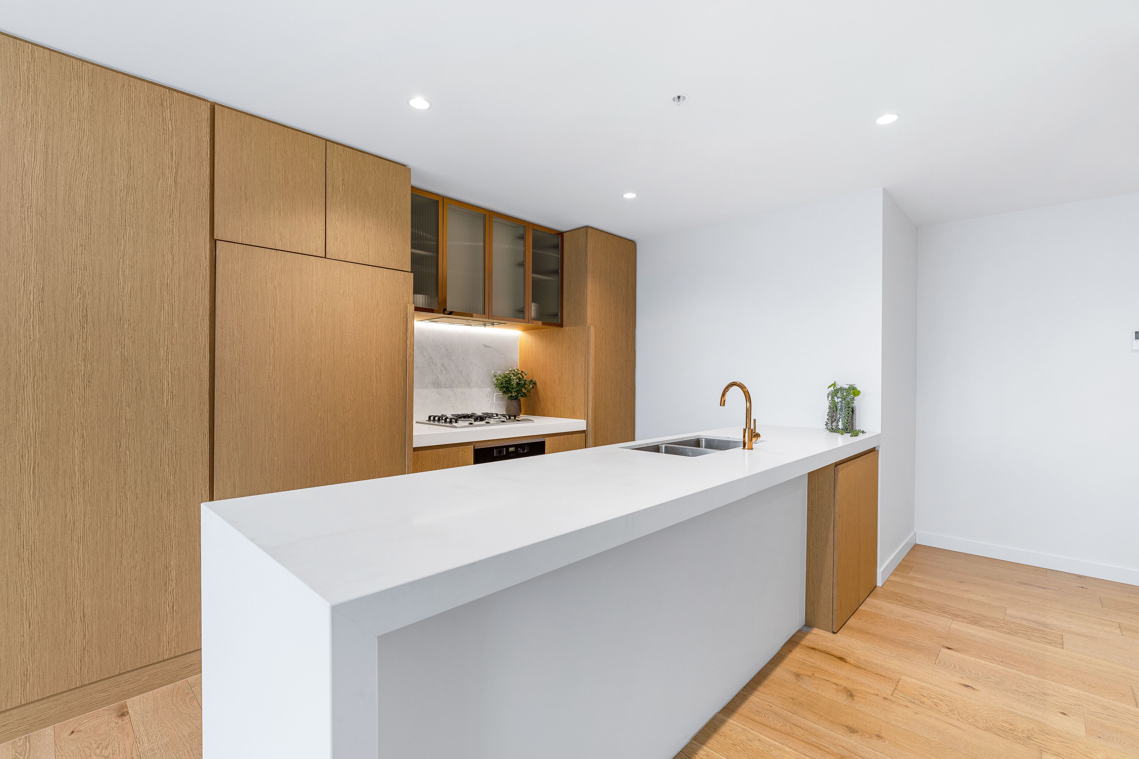 Una cocina moderna con armarios de madera, una encimera blanca y un lavamanos de acero inoxidable.