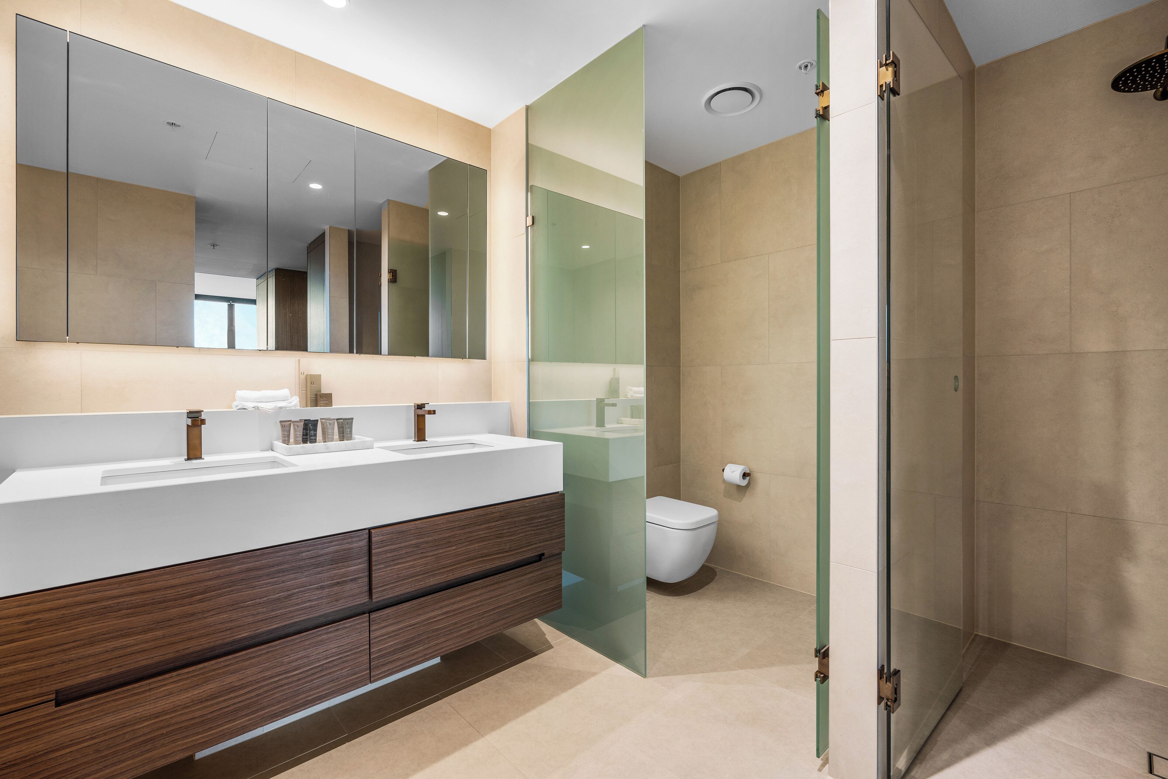 Un baño moderno con un espejo grande, lavamanos dobles y ducha con mampara de vidrio.