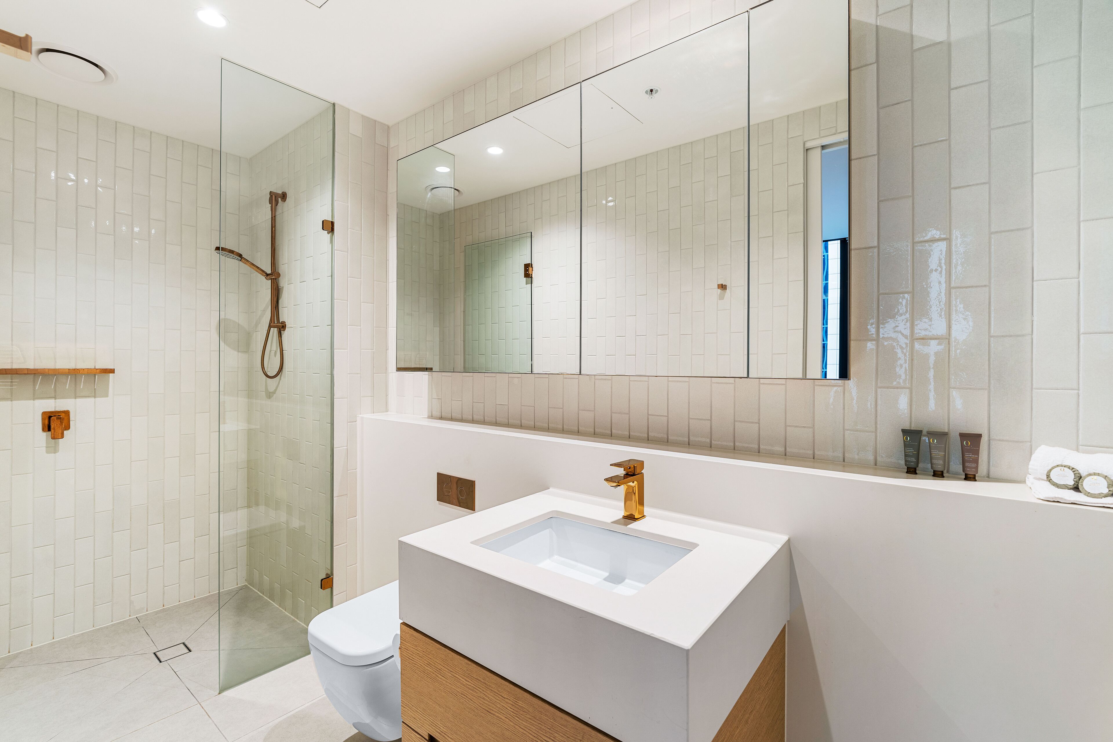A modern bathroom with a glass-enclosed shower, a white sink with a gold faucet, and a large mirror above the sink.