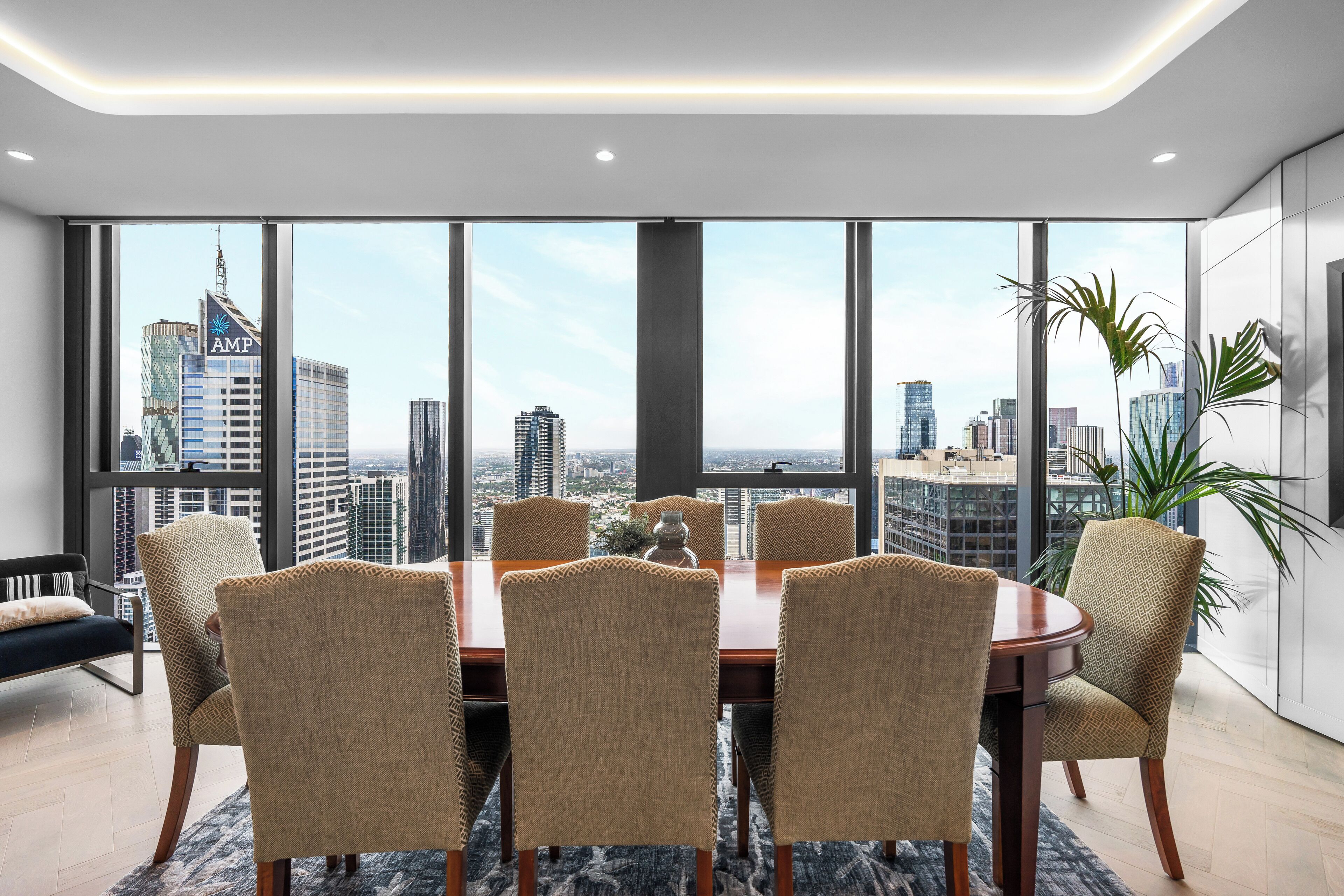A modern dining area with a large table and chairs, large windows offering a city view, and a minimalist interior design.